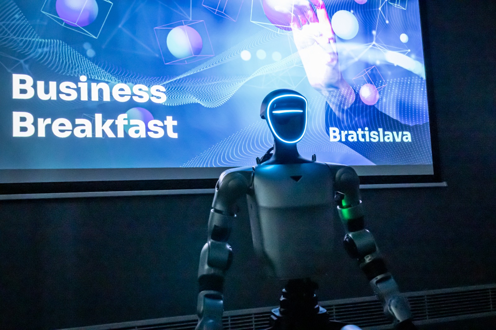 Humanoid robot in front of a Business Breakfast Bratislava screen